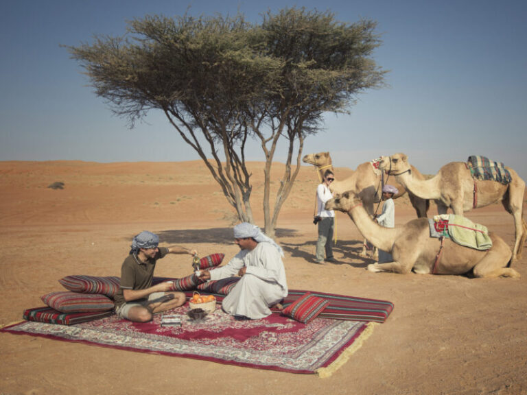 Omanische Männer und Touristen trinken arabischen Kaffee in der Wüste im Oman